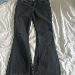 Svarta bootcut jeans med rå kant - Snygga svarta jeans med bootcut-modell och rå, fransad kant nertill. Jeansen har klassisk femficksdesign och är tillverkade i denim. Perfekta för dig som gillar en retro vibe och vill sticka ut lite extra.