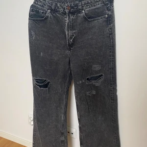 Svarta slitna jeans från Divided H&M - Svarta jeans från Divided H&M med slitningar på båda benen. Materialet är denim i bomull och färgen är tvättad svart. Går att fråga om prissänkning.
