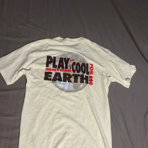 Vit loose fit Nike t-shirt med tryck - Vit t-shirt från Nike i loose fit med klassisk logga framtill och stort tryck på ryggen med texten 'Play it cool for Mother Earth'. Skön bomullskvalitet och korta ärmar, perfekt för en chill och avslappnad stil.