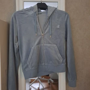 Ljusblå  hoodie Juicy Couture - Supermjuk ljusblå hoodie från Juicy Couture  med dragkedja, huva och snörning. Klassisk logga broderad på bröstet och känguruficka framtill. Perfekt för chill dagar eller när du vill ha en mysig look. Lappar klippborta.