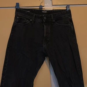 Svarta relaxed jeans från Jack & Jones - Svarta jeans från Jack & Jones i relaxed fit-modellen Chris. Klassisk femficksdesign, knäppning med knappar och raka ben. Jeansen är tillverkade i bomull och har en mörk tvätt som ger en cool vibe.