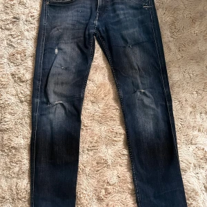 Replay anbass jeans - Snygga mörkblå jeans med slitningar på knäna och lätt tvättad look. Modellen är slim med smal passform och klassiska fem fickor. Perfekta för dig som gillar grischstilen.