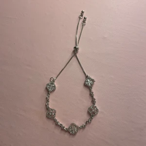 Silverfärgat armband  - Ett stilrent armband i silverfärg med fem fyrkantiga länkar, var och en dekorerad med ett blommönster och små gnistrande stenar. Justerbar kedja med kulor för perfekt passform. Perfekt accessoar för att lyfta din outfit.