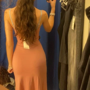 Rosa långklänning från Bershka - Säljer en snygg rosa långklänning från Bershka med smala axelband och figurnära passform. Klänningen har en enkel och stilren design, perfekt för dig som gillar minimalistiskt mode. Materialet känns mjukt och följsamt mot kroppen.