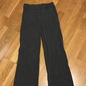 Grå /vita randiga kostymbyxor - Snygga svarta kostymbyxor med tunna vita ränder. Byxorna har raka ben och klassisk passform, perfekta för en stilren look. De har hällor för bälte och är tillverkade i ett mjukt tyg som känns bekvämt hela dagen.