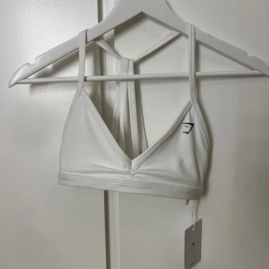 Sport-Bh Gymshark vit - En vit sport-Bh från Gymshark, aldrig använd och har prislapp kvar. Storlek Xs med light support. Banden i ryggen går att ta av så man får öppen rygg. 