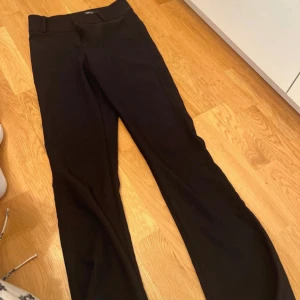 Svarta bootcut kostymbyxor - Svarta kostymbyxor med bootcut-snitt och snygga fickor med lock och knappar bak. 