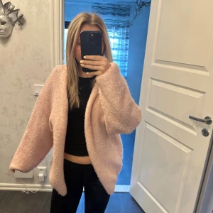 Ljusrosa stickad kofta från Lindex - Supermysig och oversized ljusrosa stickad kofta från Lindex. Koftan har lång ärm, öppen framtill och är gjord i ett fluffigt, mjukt material. Perfekt att slänga på sig när det är kyligt ute.