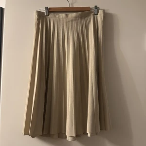 Beige plisserad långkjol i linne - Snygg beige plisserad långkjol i linneblandning. Kjolen har klassiska veck och en mjuk, flowy känsla som ger en stilren och tidlös look. Perfekt för dig som gillar minimalistisk och clean stil. Midjemått och längd syns på bilderna.
