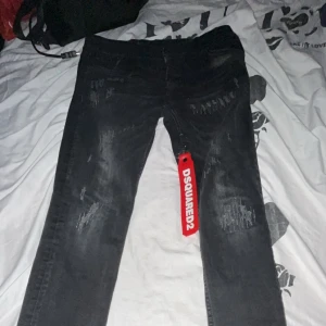Svarta Dsquared2 jeans med slitningar - Snygga svarta jeans från Dsquared2 med coola slitningar och tvättade detaljer. Klassisk femficksmodell med normal passform och tydlig Dsquared2-tag framtill. Perfekta för dig som gillar streetstyle och vill sticka ut.