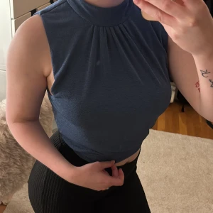 Blå ärmlös topp med öppen rygg💕 - Säljer en blå ärmlös topp med hög hals och snygga rynkdetaljer framtill. Toppen har en öppen rygg med twistad detalj och stängs med dragkedja bak. Perfekt för dig som vill sticka ut med en cool och modern look.