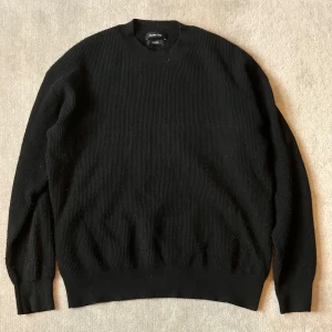 Svart ribbad stickad tröja från massimodutti - En svart stickad tröja från Massimodutti med ribbad struktur. Tröjan har rund halsringning och långa ärmar, perfekt för lager-på-lager under kyliga dagar. Enkel och stilren design som funkar till allt.