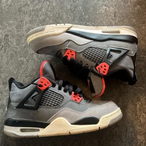 Nike Air Jordan 4 Retro Grå/Röd - Säljer ett par Nike Air Jordan 4 Retro sneakers i grå mocka med svarta och röda detaljer. Skorna har klassisk meshpanel, svarta snören och en bekväm platt sula. Perfekta för dig som gillar streetwear och vill sticka ut med en ikonisk modell.