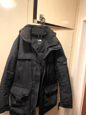 Svart parkas från The North Face (Hyvent) - Säljer en svart parkas från The North Face med flera stora fickor, huva och dragkedja framtill (Knappar för att stänga jackan) 7+1 fickor.  Jackan är hel i mycket bra skick, vadderad och har justerbara muddar med kardborre. Perfekt för kalla dagar och har en clean, funktionell look.  ”Vattentät” och otroligt värmande! Avtagningsbar luva. Verkligen stor ”S”  ( M/L som jag alltid annars har passar.  Tvättad innan försäljning.