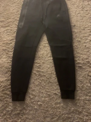 Svarta mjukisbyxor från Nike S - Svarta mjukisbyxor från Nike i storlek S. Byxorna har dragsko i midjan, ribbade muddar vid bensluten och en diskret Nike-logga på benet. Tillverkade i mjukt material som passar perfekt för chill eller träning.