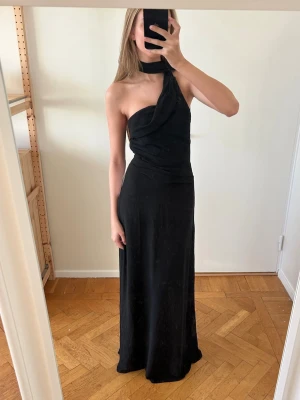 Svart långklänning - Säljer en svart långklänning scarf-liknande detalj runt halsen. Helt ny med prislapp kvar🤍