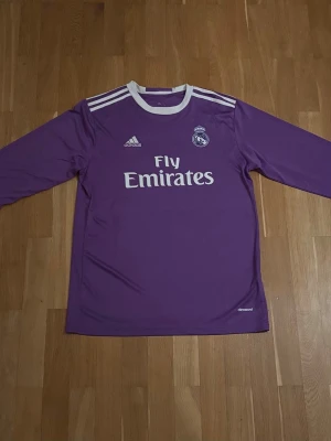 2016/2017 Ronaldo långärmad tredjetröja - Lila Real Madrid-tröja med Cristiano Ronaldo #7 på ryggen. Klassisk Adidas-design med Fly Emirates-tryck framtill och klubbemblem på bröstet. En ikonisk tröja från Ronaldos tid i Real Madrid – perfekt för både samlare och vardagsbruk.