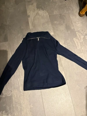 Jack and Jones halv sip hoddie - Mörkblå stickad tröja från Jack and Jones med lång ärm och ribbade muddar. Tröjan har en snygg half zip-dragkedja vid halsen som ger en sportig touch. Perfekt till höst och vinter för en clean och stilren look funkar på sommaren med.