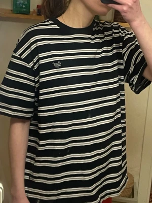 Svartvit/grå randig t-shirt från Sweet SKTBS - Säljer en svart t-shirt från Sweet SKTBS med vita och grå horisontella ränder. Oversized passform och klassisk rund hals. Broderad logga på bröstet. 