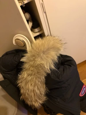 Svart Canada Goose dunjacka äkta med päls  - Säljer en svart Canada Goose dunjacka med stor huva och avtagbar beige pälsdetalj. Jackan har dragkedja, knappar och flera fickor, samt den klassiska loggan på ärmen.