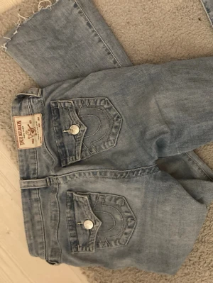 True Religion Becca Bootcut Jeans ljusblå - Ljusblå bootcut jeans från True Religion, modell Becca Mid Rise Bootcut. Klassiska fickor med lock och silverknappar bak, samt snygga sömmar. Jeansen är i mjukt denimtyg och har en midwaist passform som sitter riktigt snyggt på kroppen.