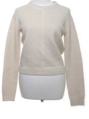 Beige stickad tröja från Zara - Säljer en beige stickad tröja från Zara med rund halsringning och en snygg söm framtill. Tröjan har långa ärmar och ribbade muddar vid ärmslut och nederkant. Perfekt för lager på lager under hösten och vintern.