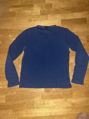 Blå långärmad tröja från BOSS - Snygg blå långärmad tröja från BOSS i slim fit-modell. Tillverkad i mjuk bomull med diskret metallogo vid nederkanten. Perfekt till jeans eller chinos för en clean och stilren look. Storlek L men passar M!