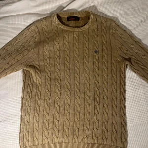 Beige kabelstickad tröja från Morris  - Säljer en beige kabelstickad tröja från Morris med rund halsringning och diskret logga broderad på bröstet. Perfekt för lager på lager under höst och vinter. Köpt för 1799.