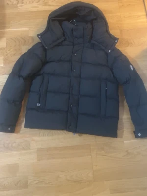 Svart Moncler dunjacka med huva -  Moncler dunjacka i svart. Helt ny och aldrig använd, fick den i present. Nypris ca 20 000 kr men säljs för 3 000 kr för snabb affär samt saknar kvitto eftersom jag fick i present. Jackan är i nyskick med alla originaldetaljer kvar. Varm, stilren och av hög kvalitet. Perfekt vinterjacka.