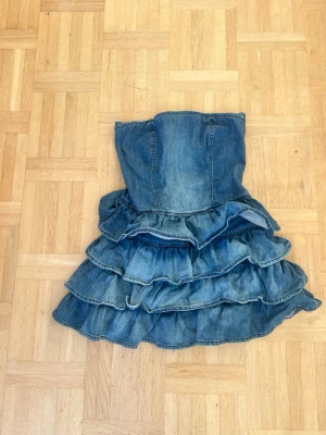 Jeansklänning med volanger💖 - Säljer en axelbandslös jeansklänning med flera lager volanger och dragkedja i ryggen. Klänningen har en cool och ungdomlig look, perfekt för dig som gillar denim och vill sticka ut. Passformen är normal och materialet är klassiskt jeans.