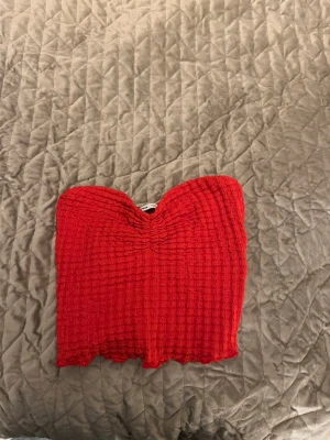 Röd bandeau tubtopp från Bershka - Säljer en röd bandeau tubtopp från Bershka i storlek XS. Toppen är smockad med vågig nederkant och har en snygg hjärtformad överkant. Perfekt för sommaren och enkel att matcha med jeans eller kjol.