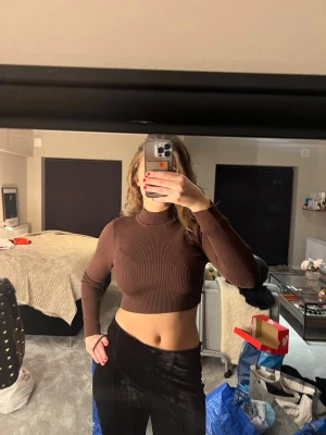 Brun ribbad croppad polotopp - Säljer en brun croppad polotopp med lång ärm. Toppen är ribbstickad och har en tight passform som framhäver figuren. Perfekt att styla med höga byxor eller kjol för en trendig look.