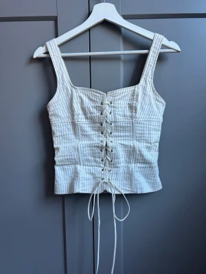 Vit randig korsettopp från Zara - Säljer en superfin korsettopp från Zara. Toppen är i superbra skick och i storlek XS. Har sytt in axelbanden något då de var väldigt långa, man annars helt som ny! 