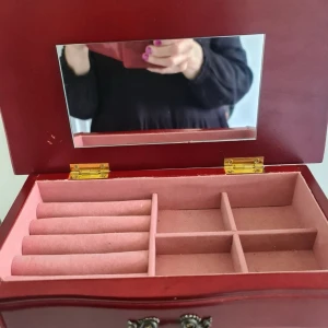 Mörkröd smyckeslåda med spegel - Säljer en snygg mörkröd smyckeslåda i trä med flera lådor och fack, perfekt för att organisera ringar, halsband och örhängen. Insidan är klädd i mjukt rosa tyg och locket har en spegel. De sista bilderna för skick! 