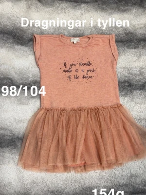 Persikofärgad tunika med tyllkjol - Supersöt persikofärgad tunika från POMPdeLUX med tryck på bröstet och fluffig tyllkjol. Toppen har korta ärmar och volangdetalj vid axlarna. Perfekt för dig som gillar dans och vill ha något extra gulligt.🌸 Dragningar i tyllen. Storlek 98/104 