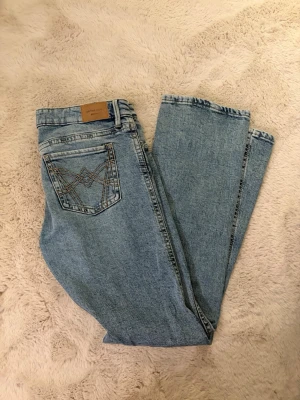 Ljusblå bootcut jeans från Perfect Jeans - Säljer ett par ljusblå bootcut jeans från gina tricot, Perfect Jeans i storlek 40. Jeansen har klassisk femficksdesign, snygga kontrastsömmar på bakfickorna och normal passform. Tillverkade i mjukt denimtyg med bälteshällor och knappgylf.