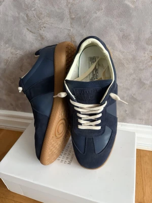 Maison margiela mörkblå st 43 - Ett par fina maison margielas. De är i storlek 43 och passar bra, skick är 8/10 lite små skador men mest creased. Haft de  lite mer än ett år annars är de bra och kommer med lådan, och kvitto (ÄKTHETSBEVIS). Skriv om du har någon fundering✅👌 