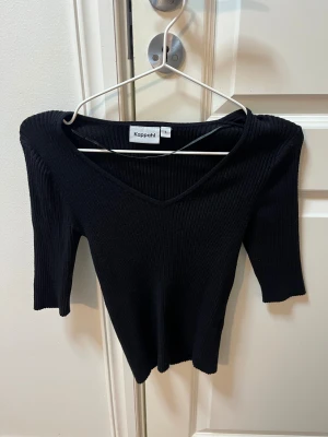 Svart ribbad topp från Kappahl - Svart ribbad topp från Kappahl med v-ringad hals och trekvartsärm. Snygg och enkel modell som är lätt att matcha till olika outfits. Materialet är stretchigt och sitter snyggt på kroppen.