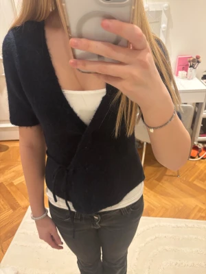 Mörkblå omlottopp från Gina Tricot - Mysig mörkblå omlottopp från Gina Tricot med korta ärmar och knyt i sidan. Toppen är stickad och har en djup v-ringning som ger en chill och trendig vibe. Perfekt att styla med jeans eller kjol för en enkel men snygg look.