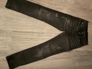 Svarta skinny jeans från Dsquared2 - Säljer ett par svarta jeans från Dsquared2. Byxorna har slitna detaljer och diskreta ljusare partier för en cool, använd look. Klassisk femficksmodell med knappgylf och Dsquared2-logga på insidan. Perfekta för dig som gillar streetstyle.