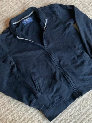 Ziptröja från Dressmann - Svart långärmad ziptröja från Dressmann i storlek M. Tröjan har ståkrage, två fickor fram och hel dragkedja. Tillverkad i mjuk bomull, perfekt för chill dagar eller när du vill ha en enkel och clean look.