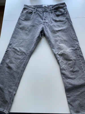Gråa jeans - Säljer ett par grå jeans från Jack & Jones, modell Relaxed Chris. De har klassisk femficksdesign, rak passform och normal midja. Materialet är slitstarkt denim i bomull och färgen är snyggt tvättad grå. Perfekt för dig som gillar avslappnad stil.