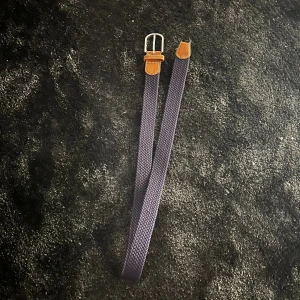 Mörkblå flätat bälte med skinn - Snyggt mörkblått flätat bälte från Globe Trotter med bruna skinn-detaljer och silverfärgat spänne. Bältet har en stilren design med präglad logga på skinnet och passar perfekt till jeans eller chinos. Flätad struktur ger en cool och modern vibe. Bältet är exklusivt hos revenite och är inte tillgängligt längre utan det finns bara 1000 tusen i världen betalet ör lite skadat men funkar mycket bra ändå 