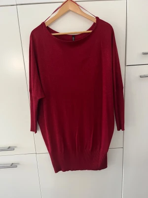 Röd loose stickad tröja från Xint - Snygg röd fin stickad tröja som kan användas som kort klänning från Xint i storlek L. Modellen är loose fit med bred ribbad kant nedtill och vid ärmslut. Tröjan har rund halsringning och långa ärmar, perfekt för dig som gillar en chill och avslappnad stil.