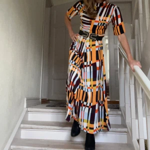 Långklänning med grafiskt mönster - Cool maxiklänning med modernt grafiskt mönster inspirerat av 50-60 tal, bl a orange och vinröd kontrastfärg. Materialet är mjukt och följsamt, härligt fall. Styla med skärp och smycken för festligare tillfällen, eller bär den till sneakers med enfärgad tröja el enklare jacka till vardag. (Obs bältet på första bilderna ingår inte i köpet). 