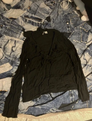 Svart bolerotopp med snörning från H&M - Svart boleroblus från H&M i storlek 32. Tunn och lätt struktur med långa ärmar och snygg snörning framtill. Toppen har en croppad passform och är tillverkad i mjuk bomull, perfekt för att ge din outfit en cool vibe.