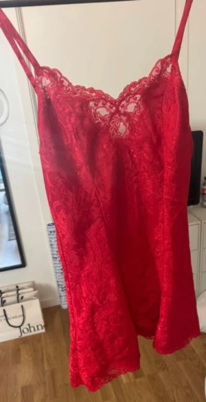 Röd spetsklänning från Victoria's Secret - Supersöt röd kortklänning från Victoria's Secret med tunna axelband och vacker spets upptill. Klänningen har ett elegant mönster i tyget och är tillverkad i polyester med spetsdetaljer i nylon. Perfekt för dig som vill sticka ut med en feminin och romantisk look.