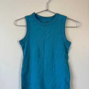 L.O.G.G. linnetopp - 134 Storlek - En turkos ärmlös linnetopp från L.O.G.G. Toppen har rund halsringning och är gjord i mjuk bomull. Enkel och stilren design. 