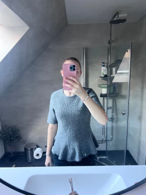 Grå stickad topp med volang - Säljer en grå stickad topp med korta ärmar och volang nertill. Toppen har rund halsringning och en mjuk, mysig känsla. Perfekt för dig som gillar en enkel men ändå söt stil.