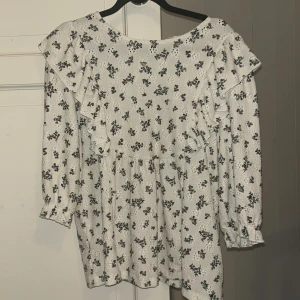 Vit blommig blus Soaked - Supersöt vit blus/topp från Soaked med små svarta blommor, volangdetaljer över axlarna och långa ärmar med resår vid handlederna. Perfekt för vår och sommar, lätt och luftig känsla. Säljes i storlek S. Köpt för 400 kr 